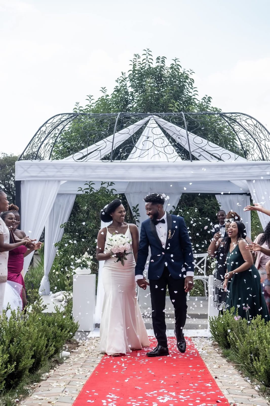 Newlyweds walking down the aisle through confetti under a garden gazebo